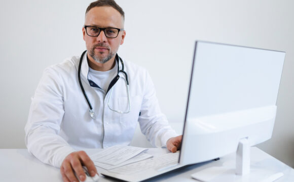 Portrait of a male doctor who works in the office at the computer Revolucionando o Acesso à Saúde com a Telemedicina